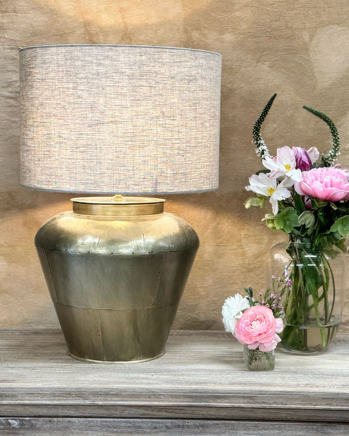 Lámpara de mesa de latón con pantalla de lino y base ancha y curva.