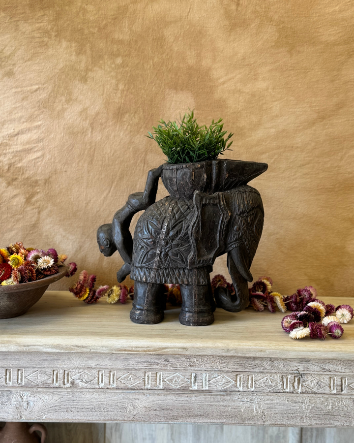 Maceta vintage con forma de elefante tallada a mano, acabado oscuro y asa con figura invertida. 