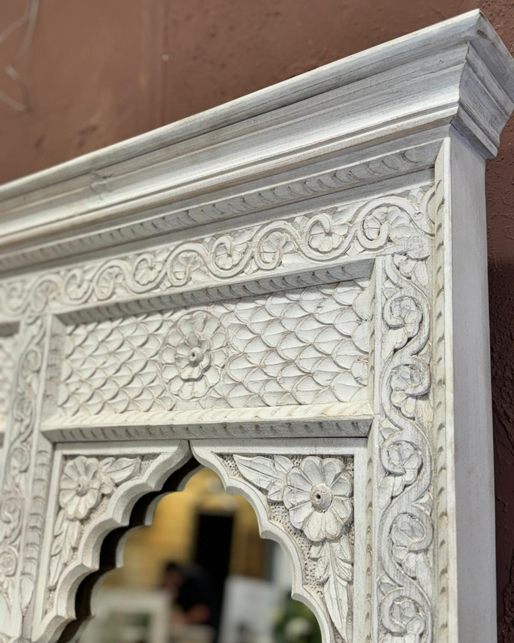 Decorative white wall mirror with intricate carvings on a brown background