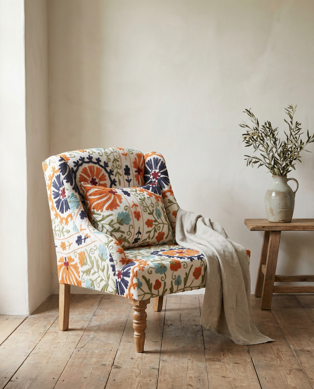 Patterned armchair in a room with a wooden floor and a small table with a vase.